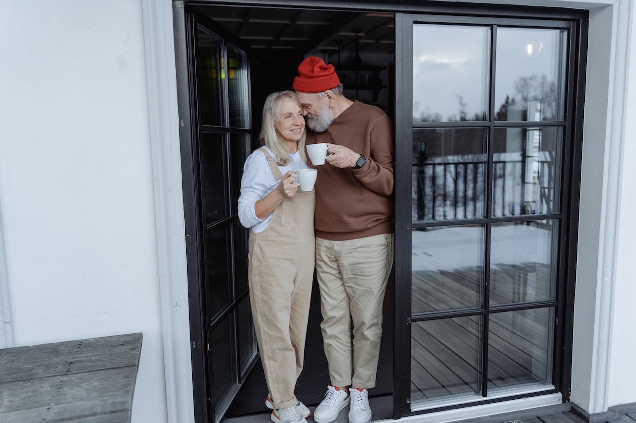 pareja mayor de pie junto a la puerta con tazas